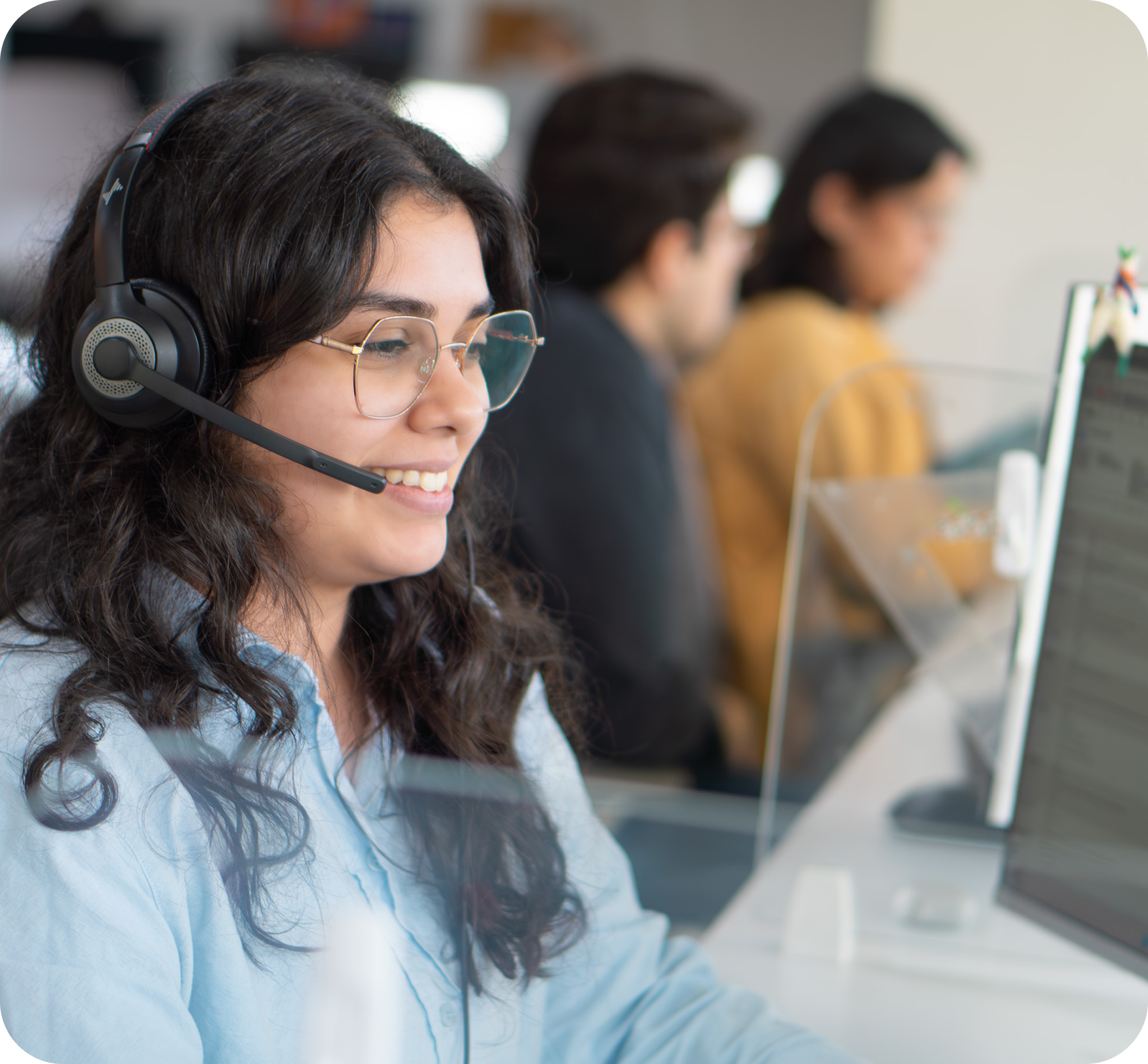 A bilingual Work Ninjas call agent wearing a headset, smiling at her screen with the team bullpen blurred behind her
